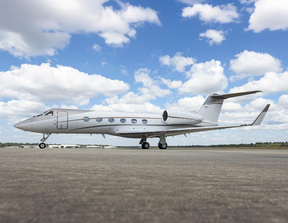 Gulfstream G550 de perfil no pátio sob céu com nuvens